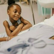 Young African American girl holding the hand of a woman in a hospital bed.