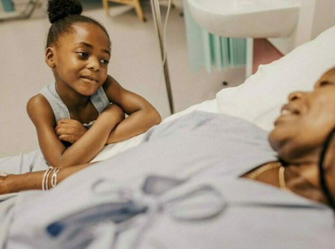 Young African American girl holding the hand of a woman in a hospital bed.