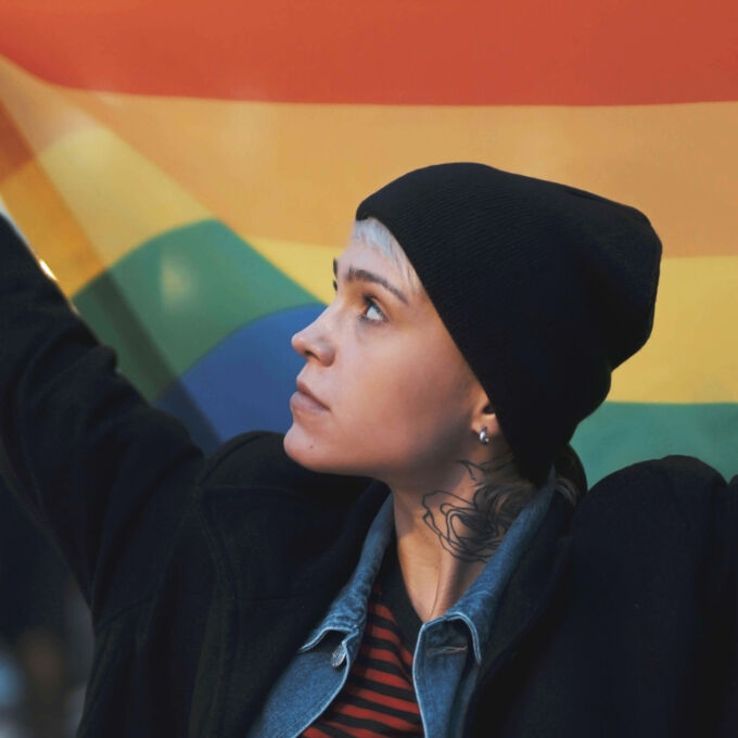 Mujer con sombrero negro sosteniendo una bandera del Orgullo LGBTQIA arcoíris.