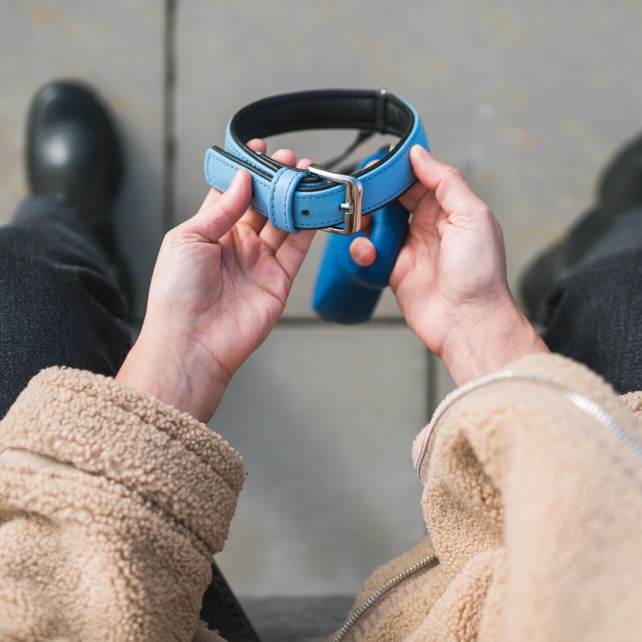 Point-of-view photo of hands holding a dog collar, looking at the sidewalk.