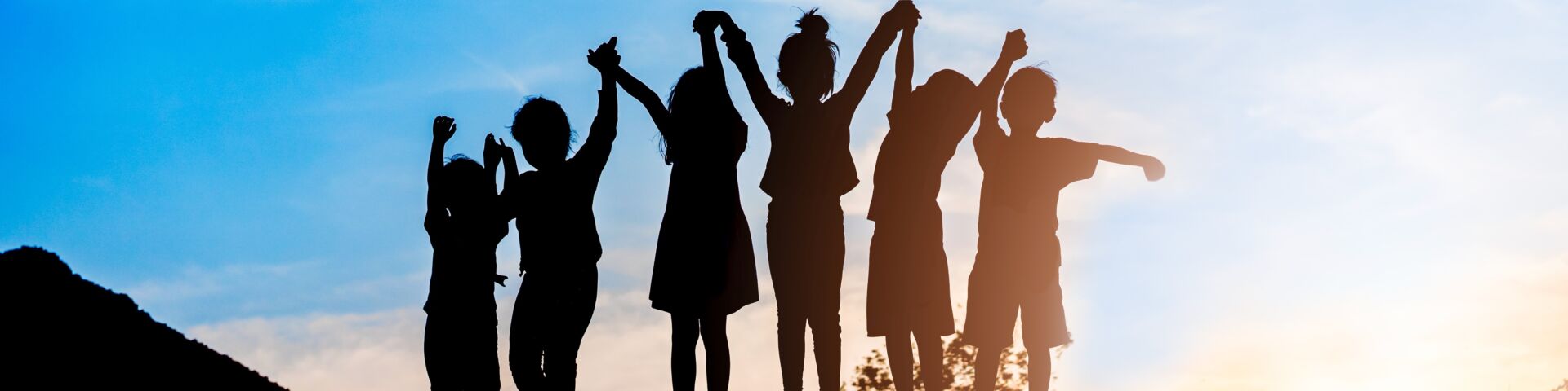 Grupo de seis niños tomados de la mano en silueta contra un cielo azul