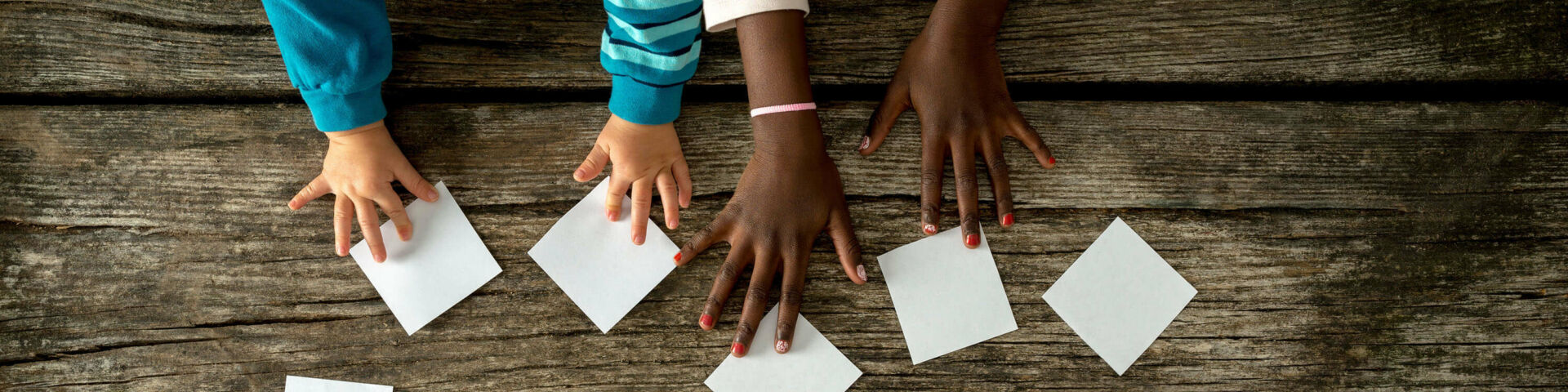 Manos de niños sobre una mesa usando tarjetas de papel para formar un corazón