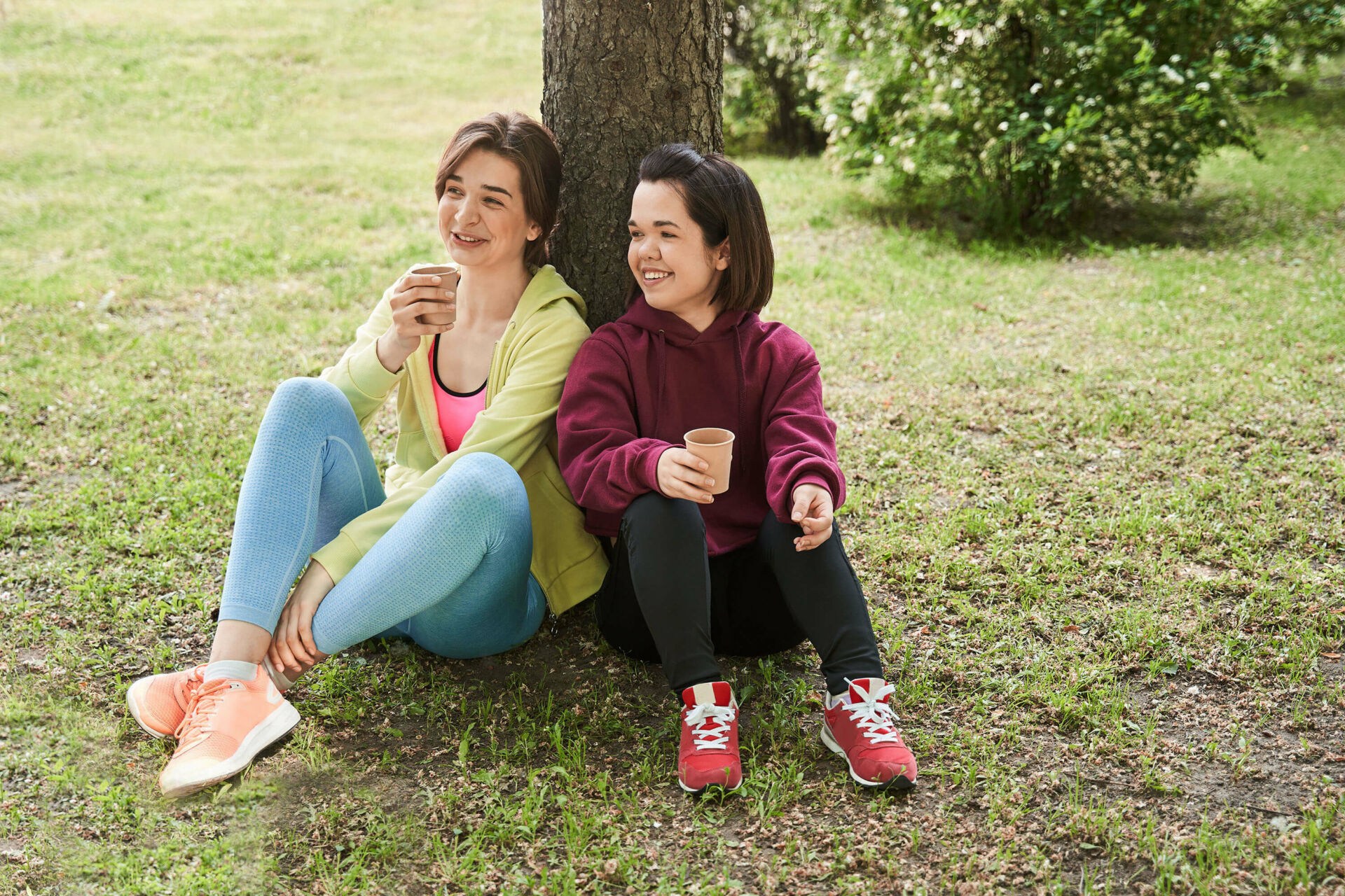 TwoWomenLeaningAgainstTreeDrinkingCoffee_