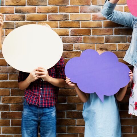 Dos niños sosteniendo carteles de papel que indican burbujas de palabras