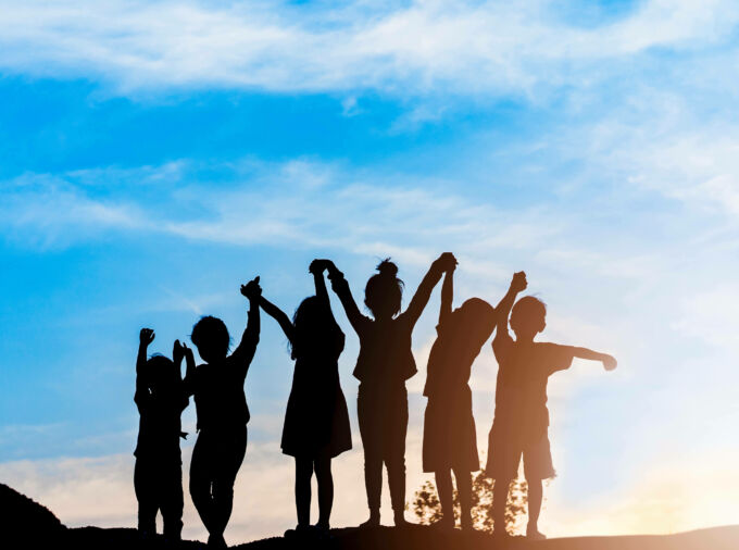 Grupo de seis niños tomados de la mano en silueta contra un cielo azul