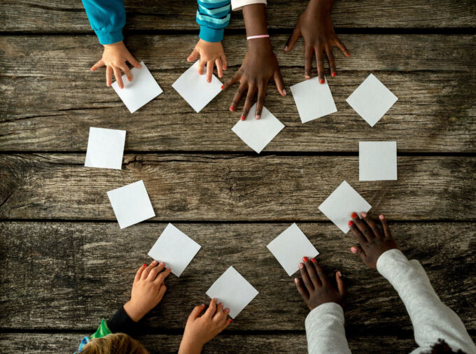 Manos de niños sobre una mesa usando tarjetas de papel para formar un corazón