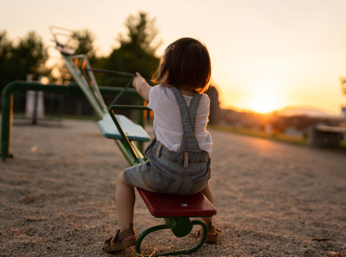 Niña sola en el sube y baja mientras se pone el sol