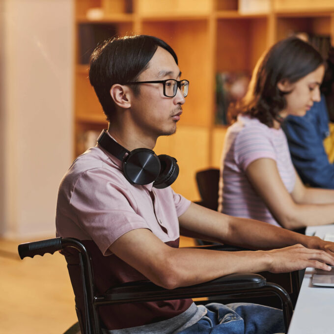 Hombre asiático en silla de ruedas sentado frente a una computadora portátil.