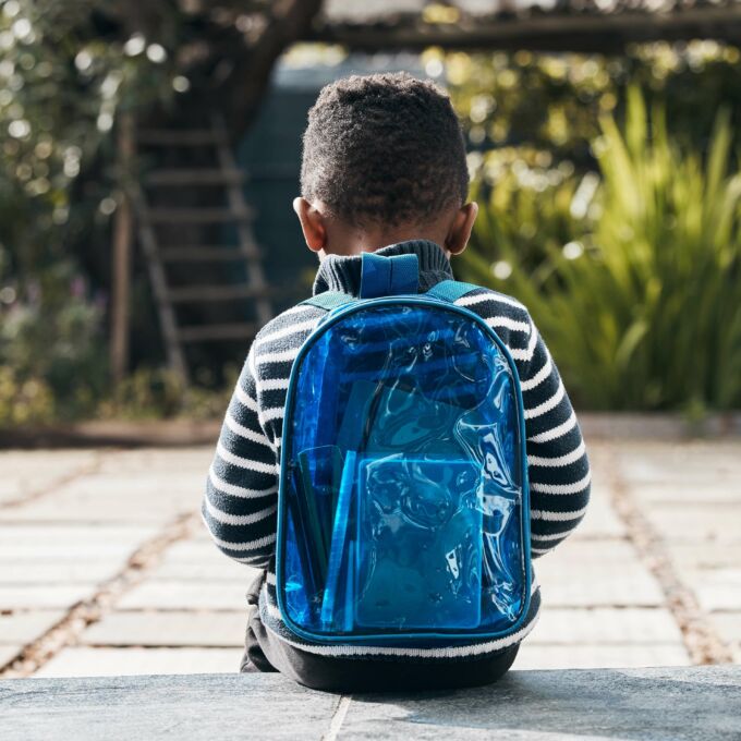 Niño pequeño con mochila azul sentado en el suelo