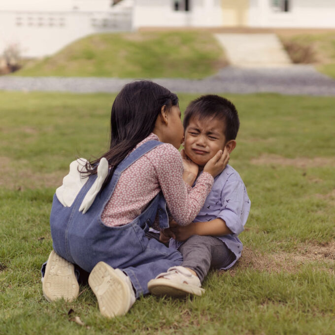 Niña en cuclillas junto a un niño pequeño que llora y lo besa en la mejilla.