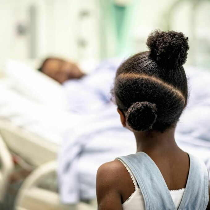 Desde atrás de una joven afroamericana mientras mira a una mujer afroamericana en la cama del hospital.