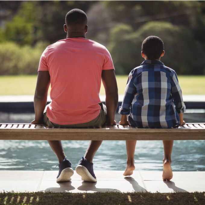 Adult sitting with kid on a bench, faced away from camera.