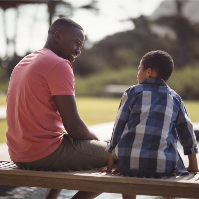 Adult and kid talking outdoors on a bench, facing each other.