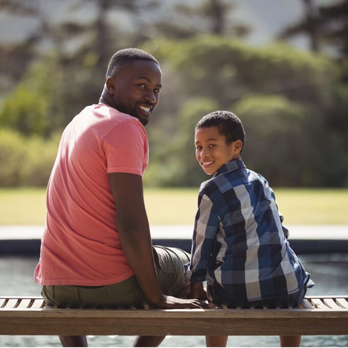 Adult and child sitting on bench together looking back at camera.